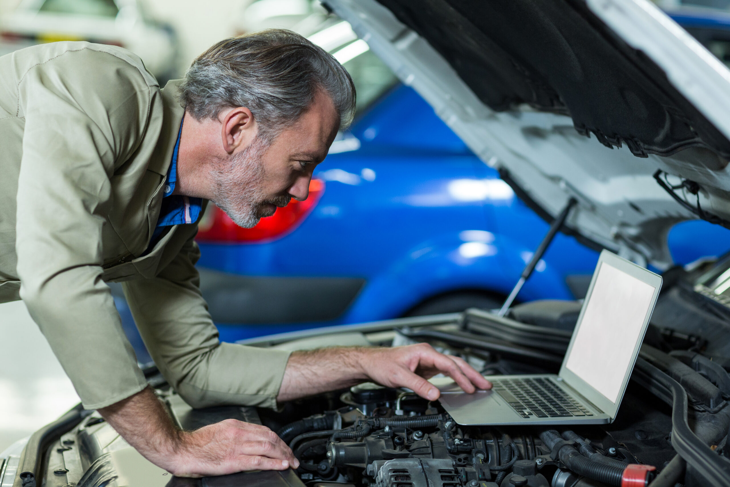 mechanic using laptop while servicing car engine